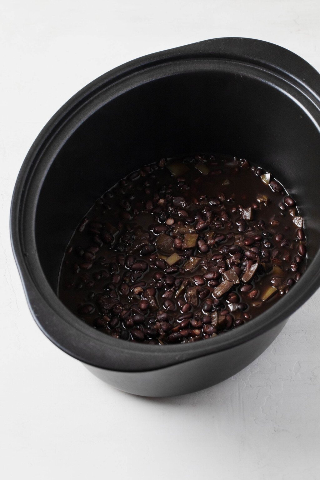 The oval-shaped, black ceramic container of a slow cooker has been used to cook black beans from scratch.