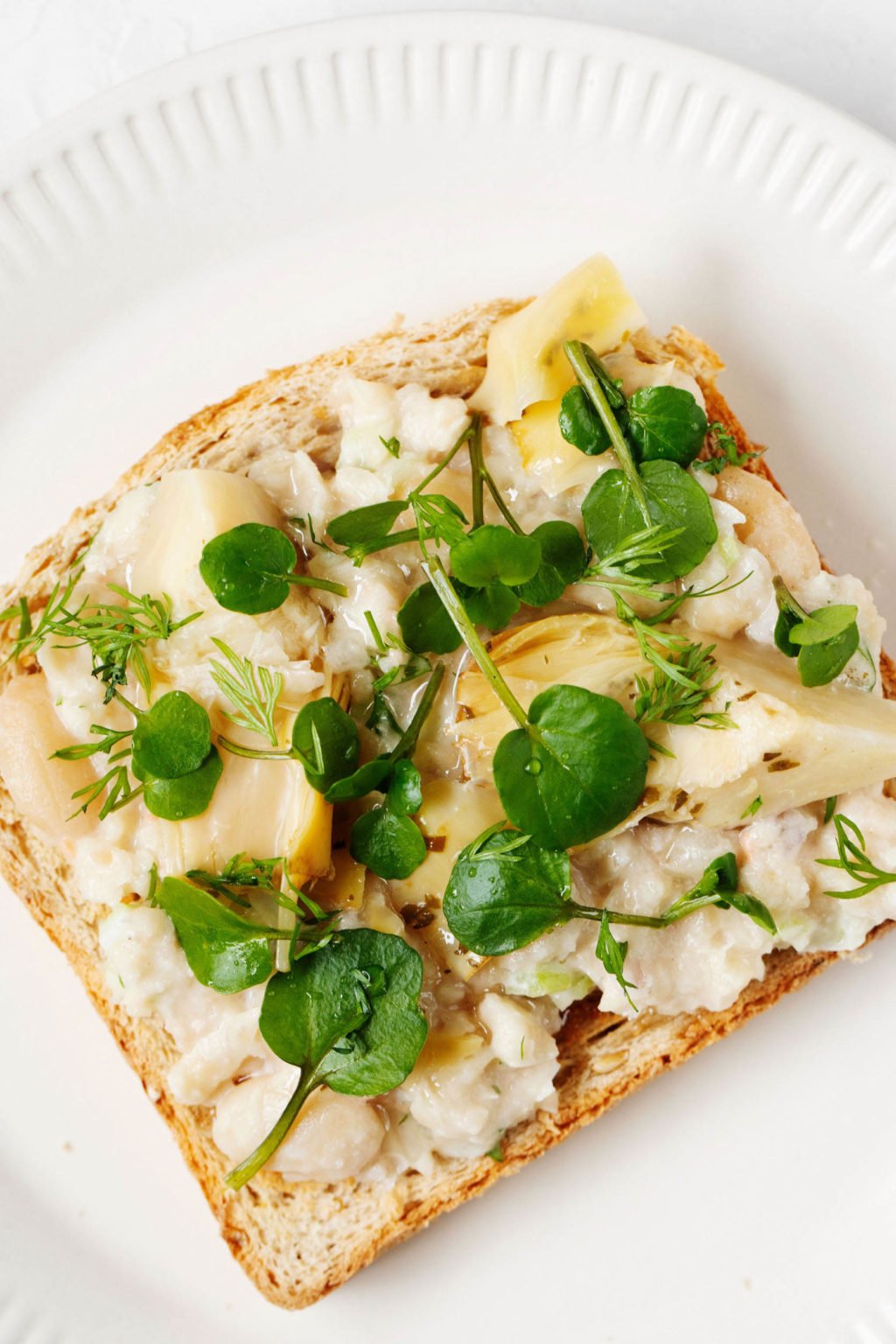 A slice of toast is topped with smashed white bean salad, artichokes, and microgreens.