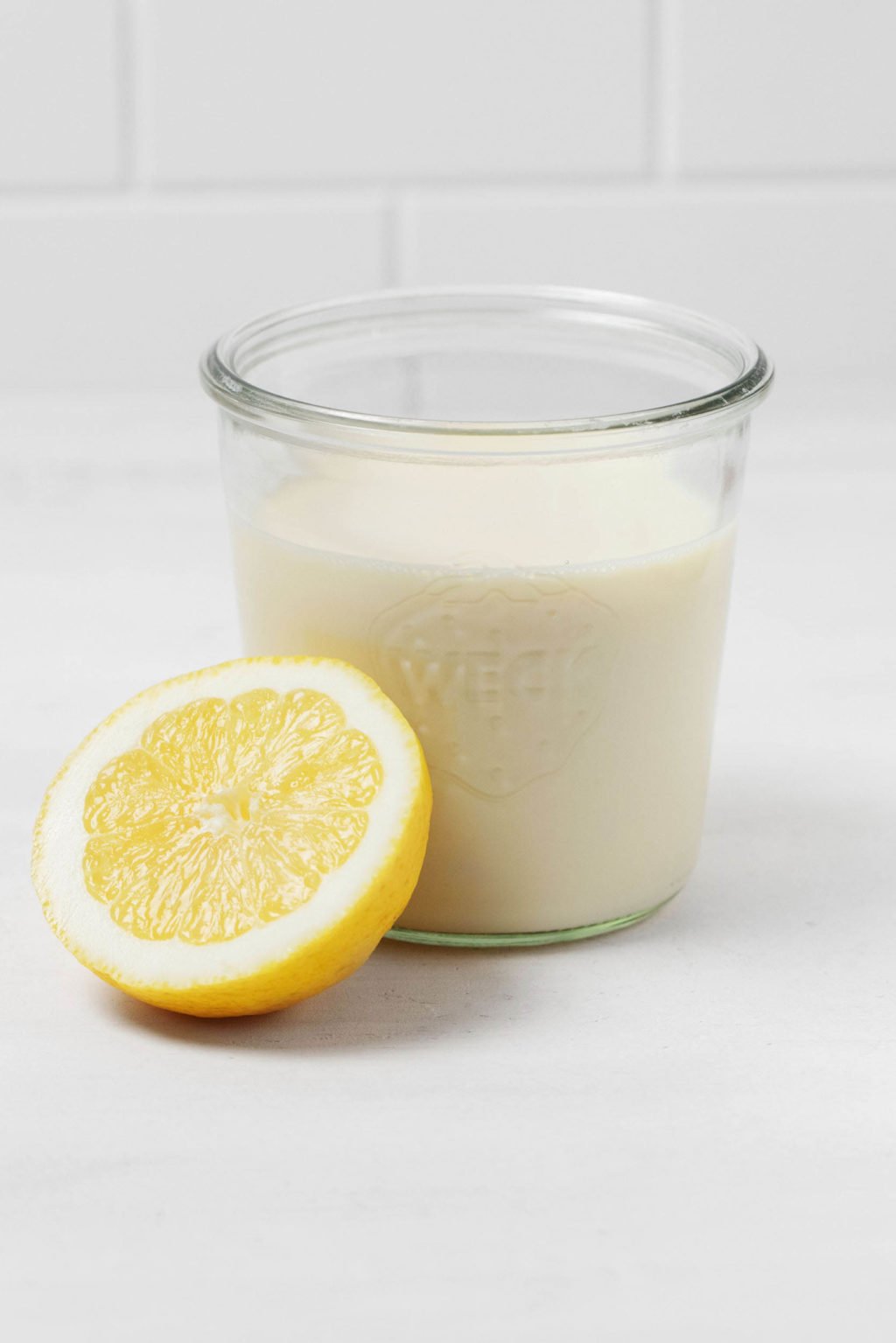 De helft van een gesneden citroen ligt naast een glazen pot gevuld met veganistische melk.