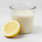 Half of a cut lemon is resting next to a mason jar full of vegan milk.