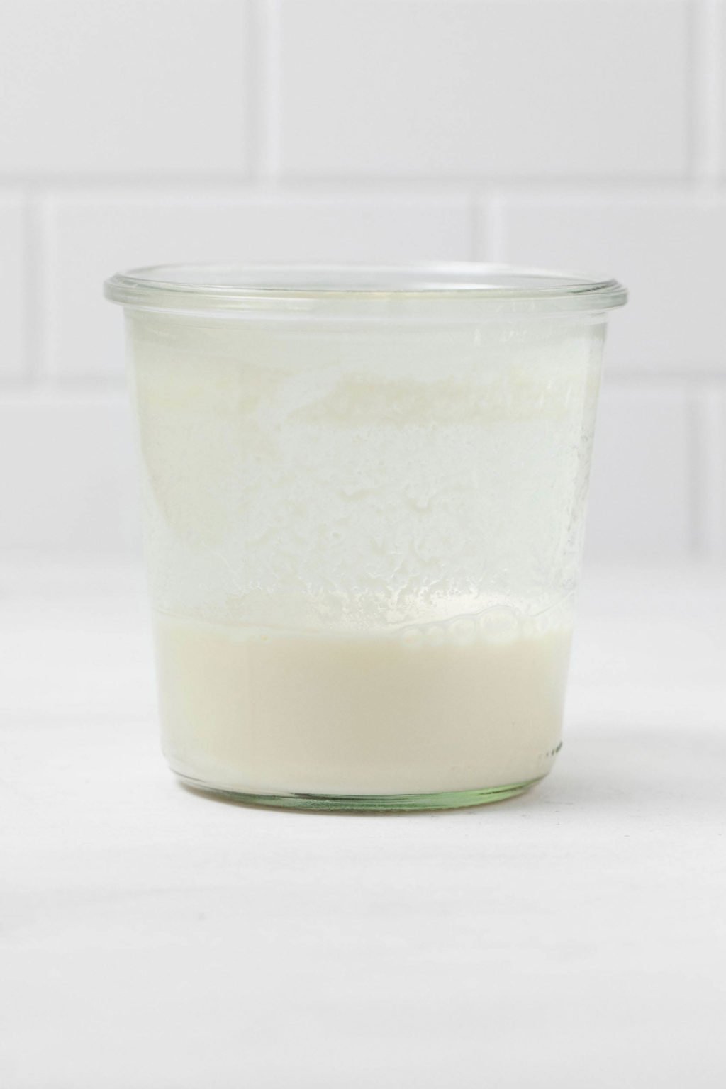 A glass jar of homemade vegan buttermilk rests on a white surface.
