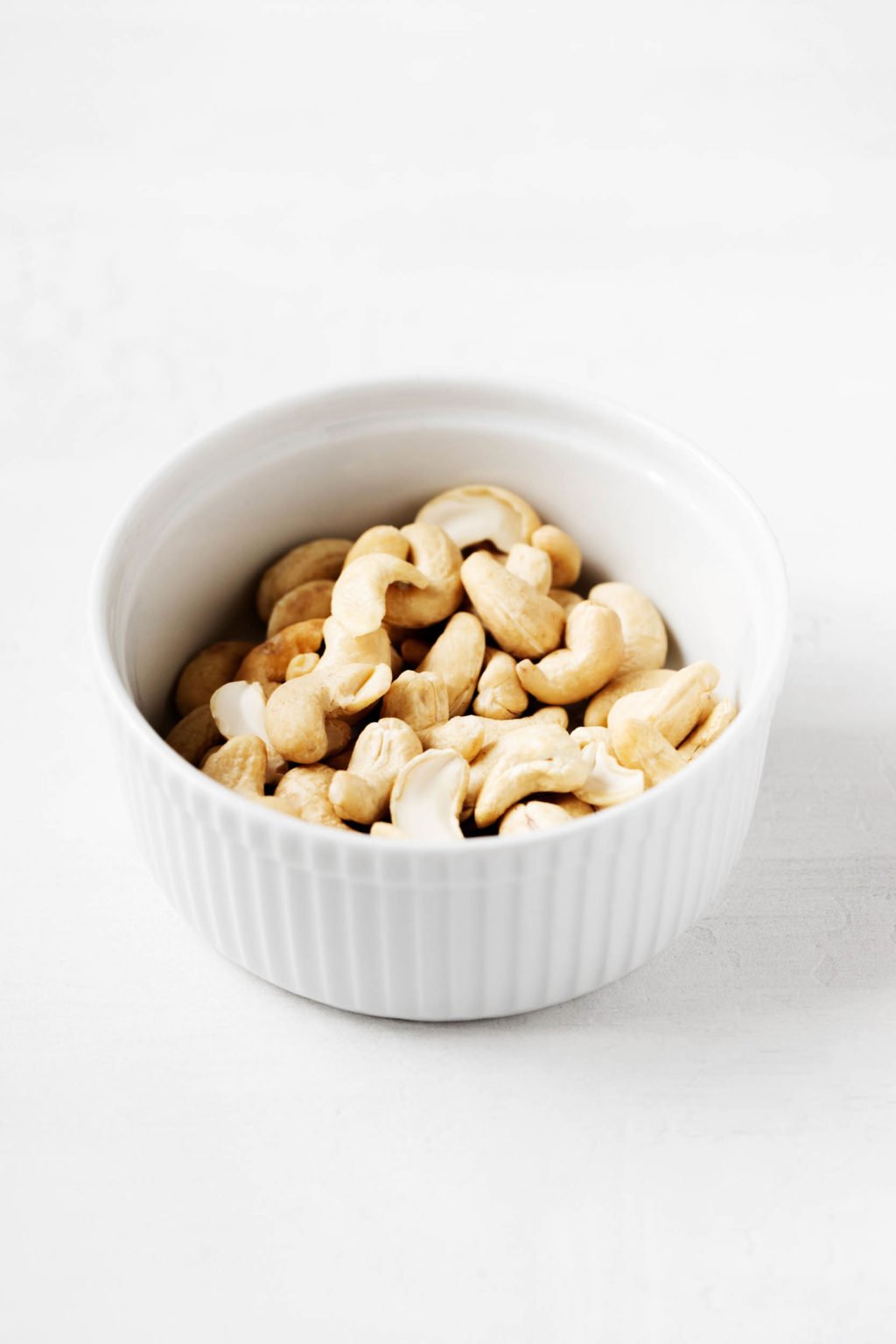 A small, white ramekin is filled with raw cashews.