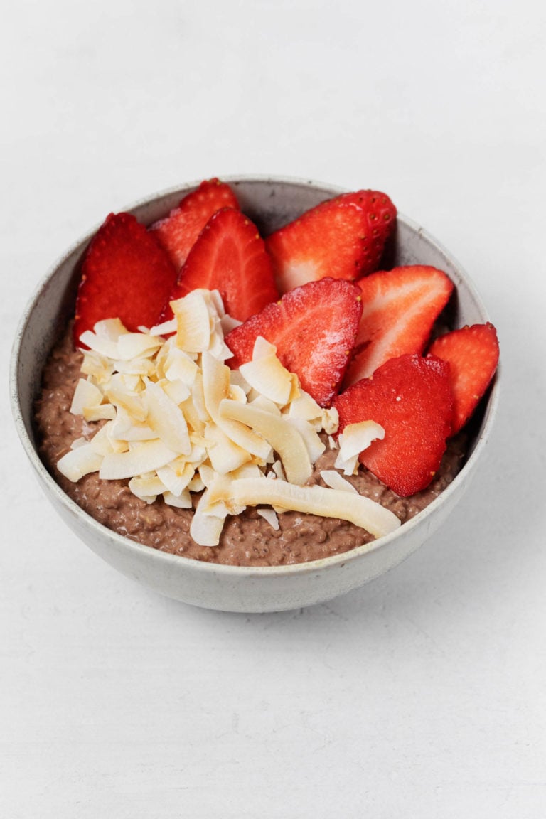 A round, ceramic bowl containing a chocolate and quinoa breakfast bowl is resting on a white surface.