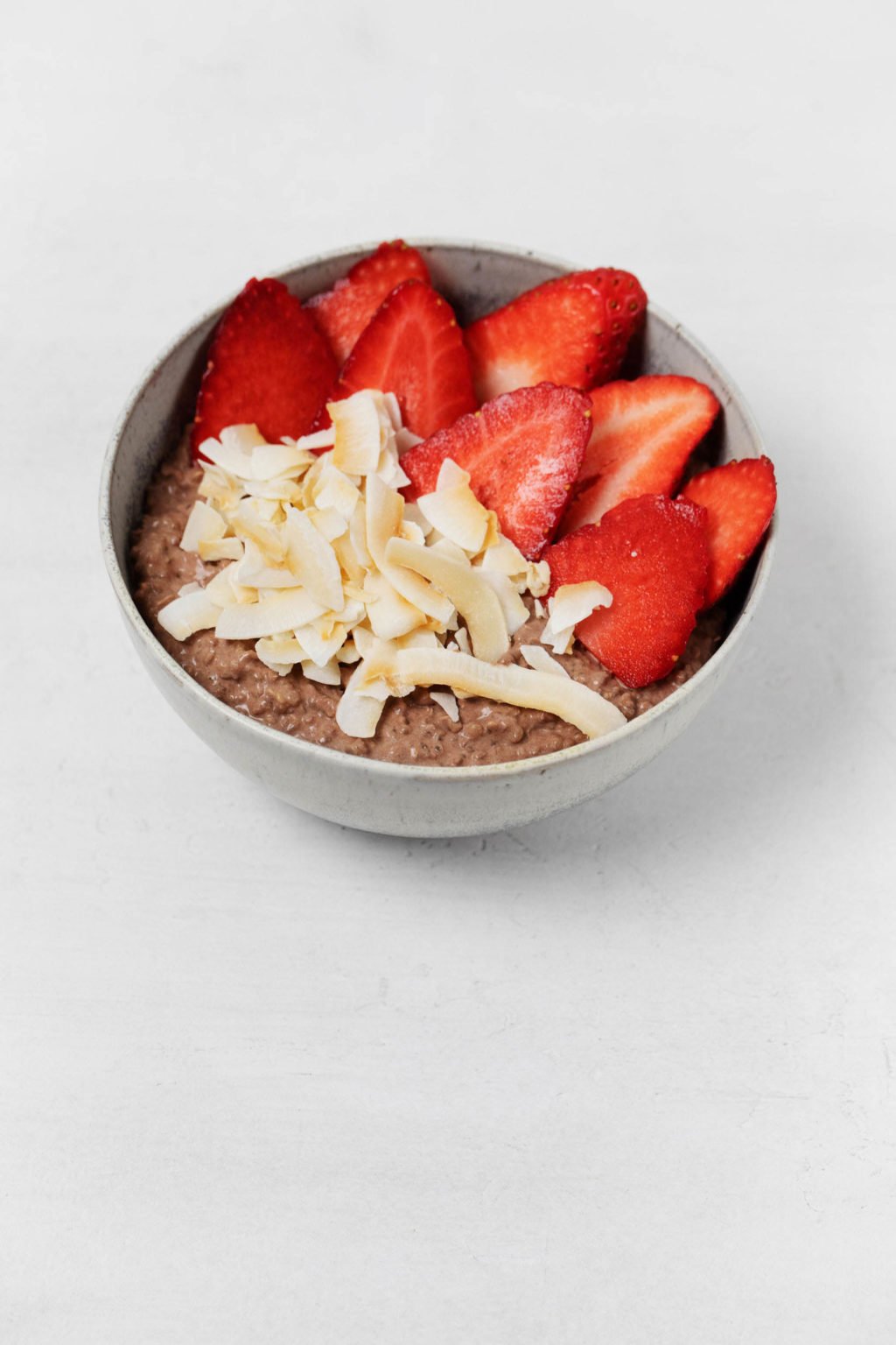 A quinoa breakfast bowl is served in a gray, ceramic bowl. It's topped with bright red, sliced strawberries.