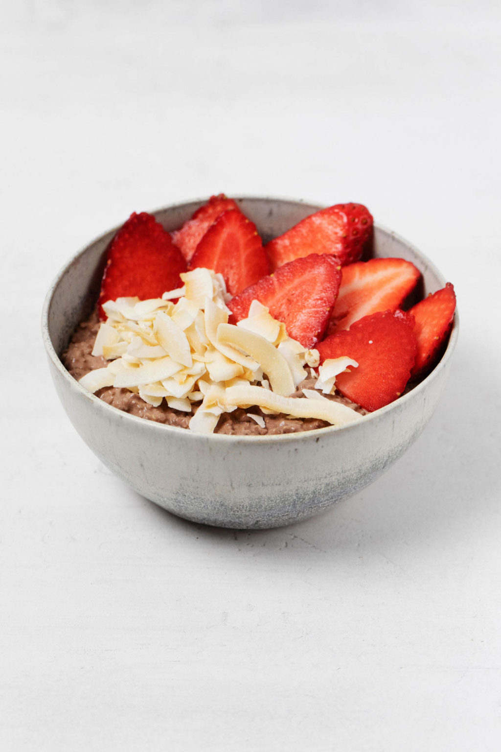 A gray, ceramic bowl contains fresh berries, coconut flakes, and chocolate-infused whole grain.