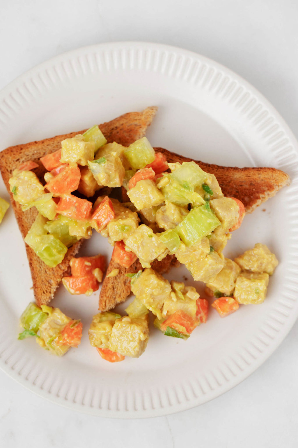 Two triangular slices of toast are topped with an easy tempeh lunch salad. 