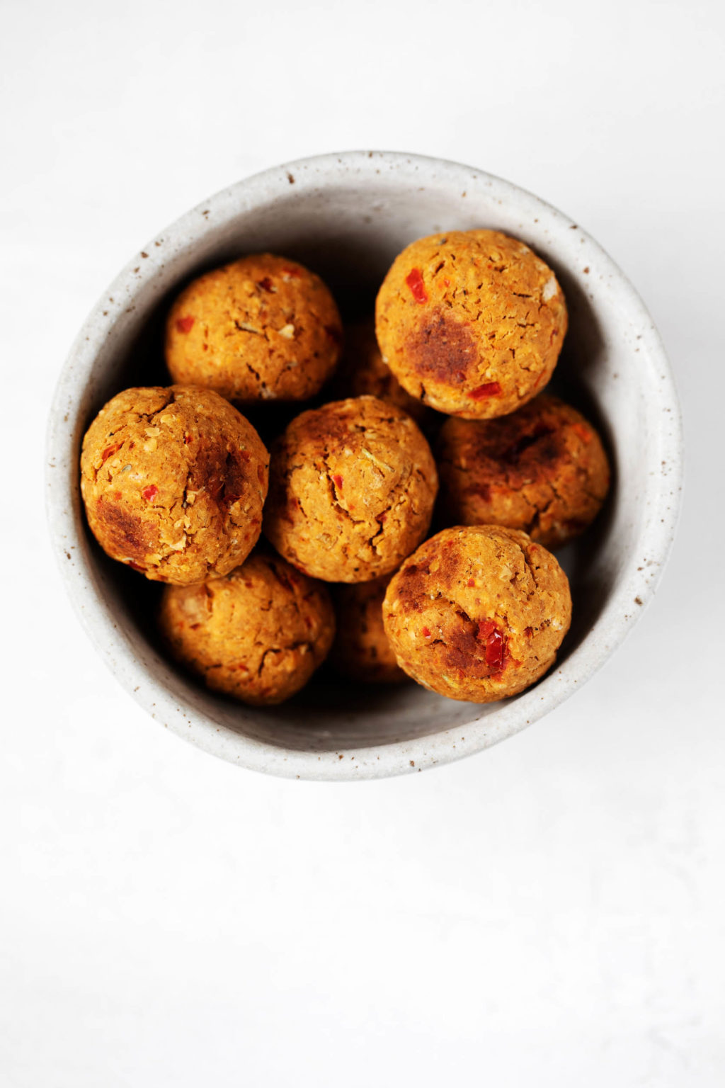 A small white ceramic bowl holds some plant-based, savory meatballs made with chickpeas and oats.