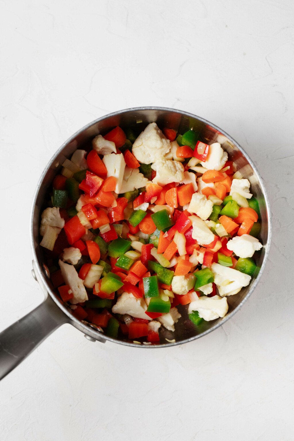 An overhead image of a bowl with peppers, cauliflower, and carrots.