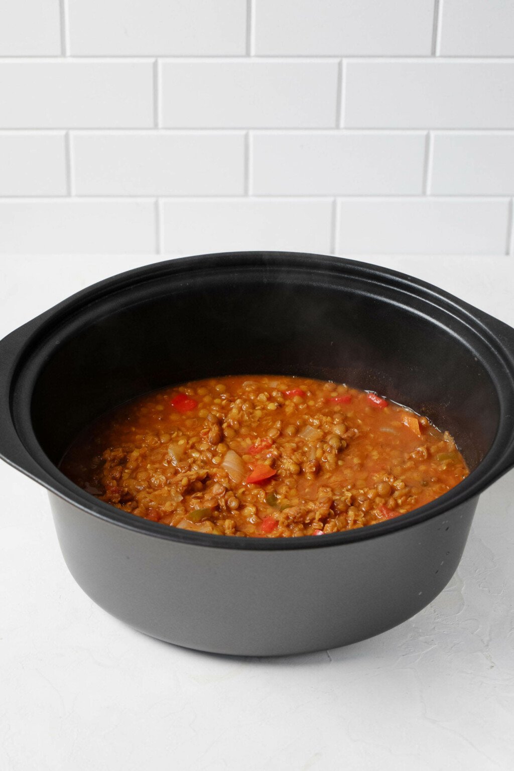 The black, oval-shaped bowl of a slow cooker is filled with a vegan chili. 