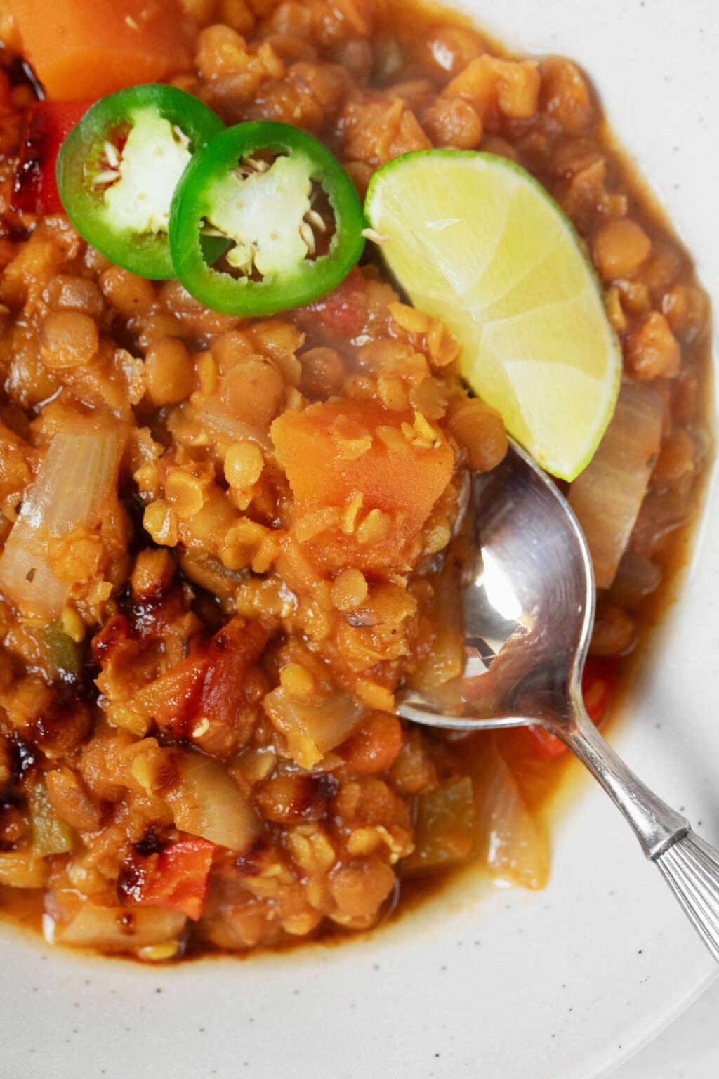 An overhead, close-up image of an orange-hued lentil chili that's being eaten with a spoon.