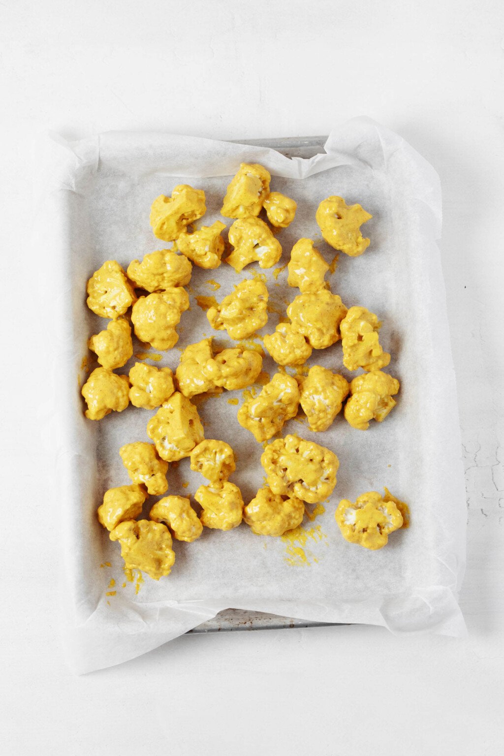 An overhead image of spice-coated cauliflower florets on a white parchment-lined baking sheet. 