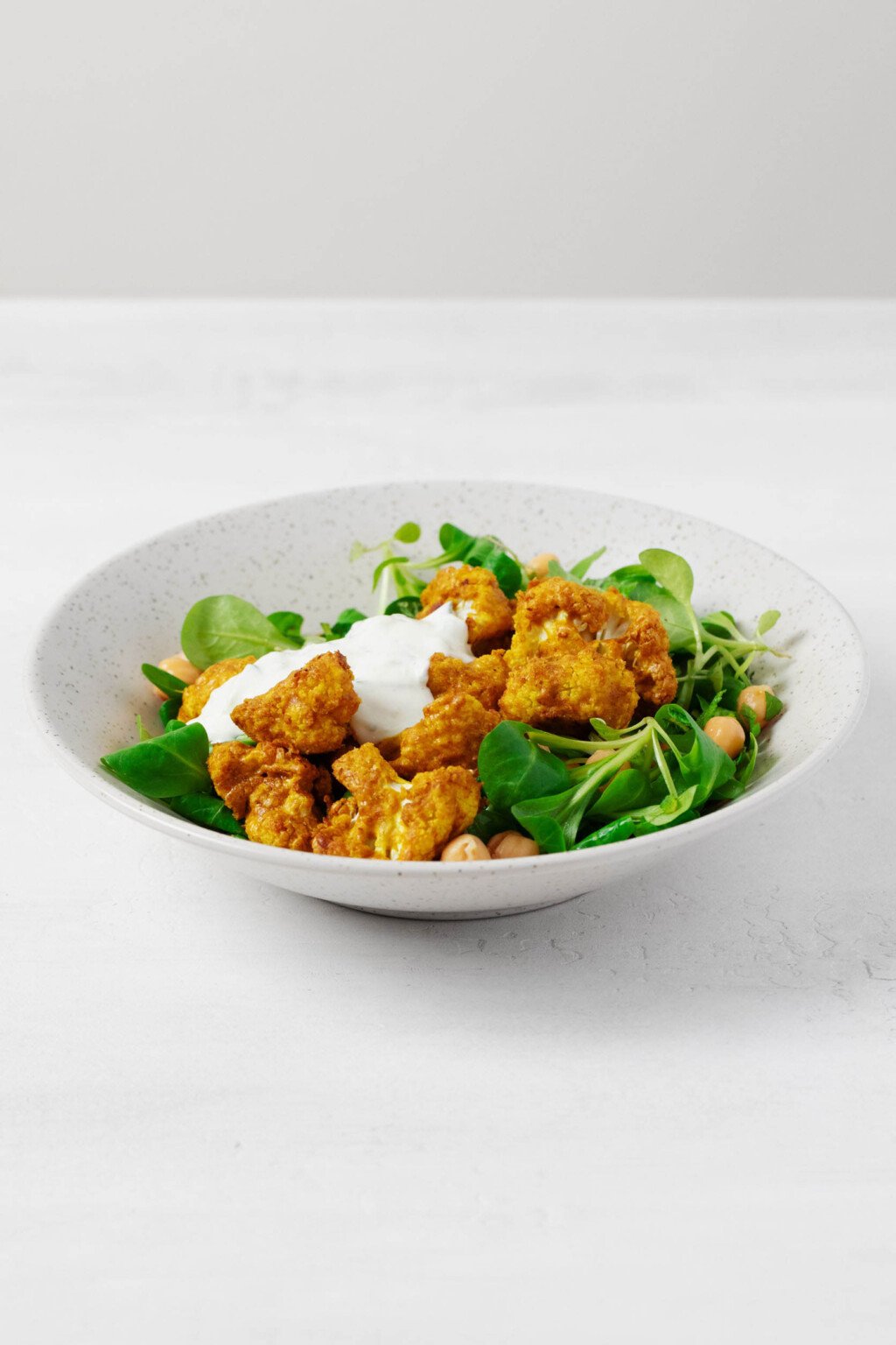 An overhead image of a bed of greens topped with tandoori spiced cauliflower, chickpeas, and a creamy sauce.