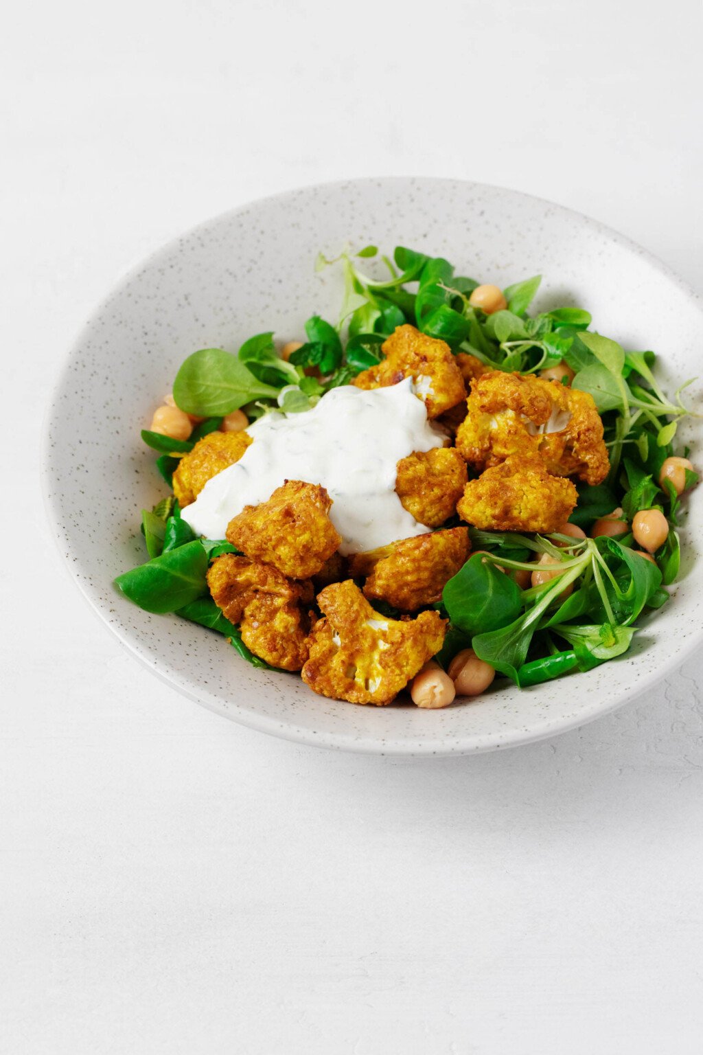 An overhead image of a bed of greens topped with tandoori spiced cauliflower, chickpeas, and a creamy sauce.