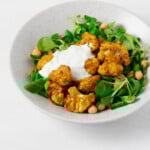 An overhead image of a bed of greens topped with tandoori spiced cauliflower, chickpeas, and a creamy sauce.