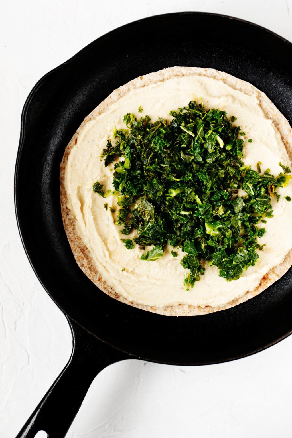 A tortilla is being heated up in a black, round skillet with plant-based ingredients.