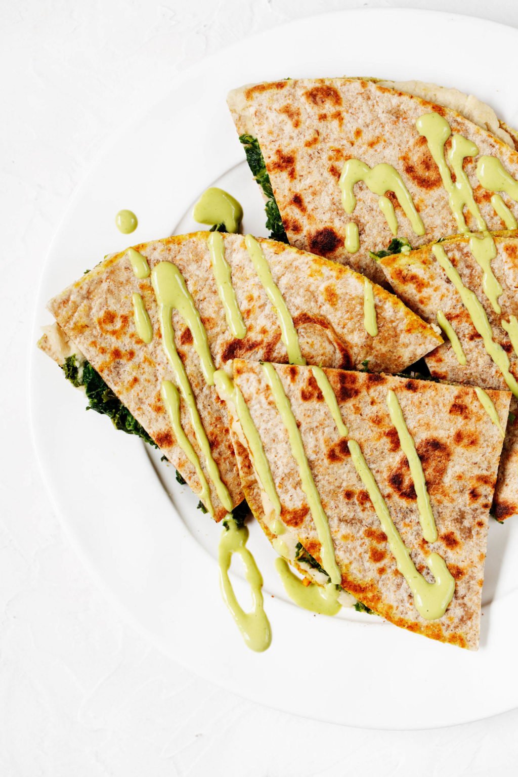 An overhead image of artichoke white bean wraps, which have been cut into triangle shapes and garnished with a green sauce.