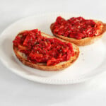 Two oval-shaped slices of toast are topped with a bright red cherry tomato jam.