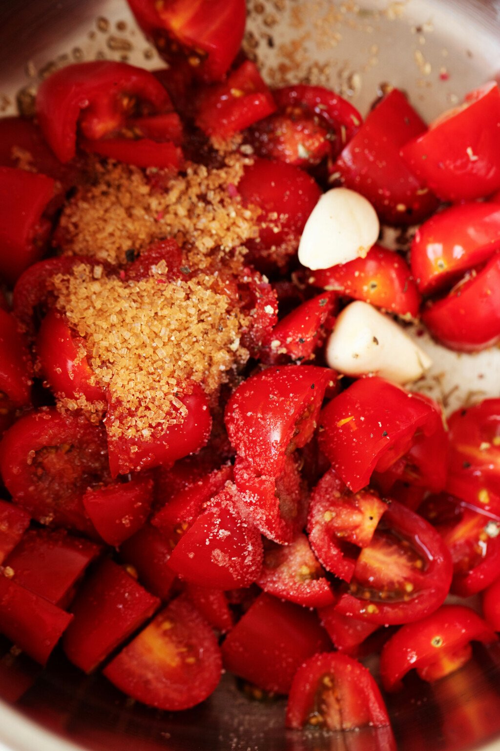 Halved grape tomatoes, garlic, sugar, and other ingredients are photographed from overhead.