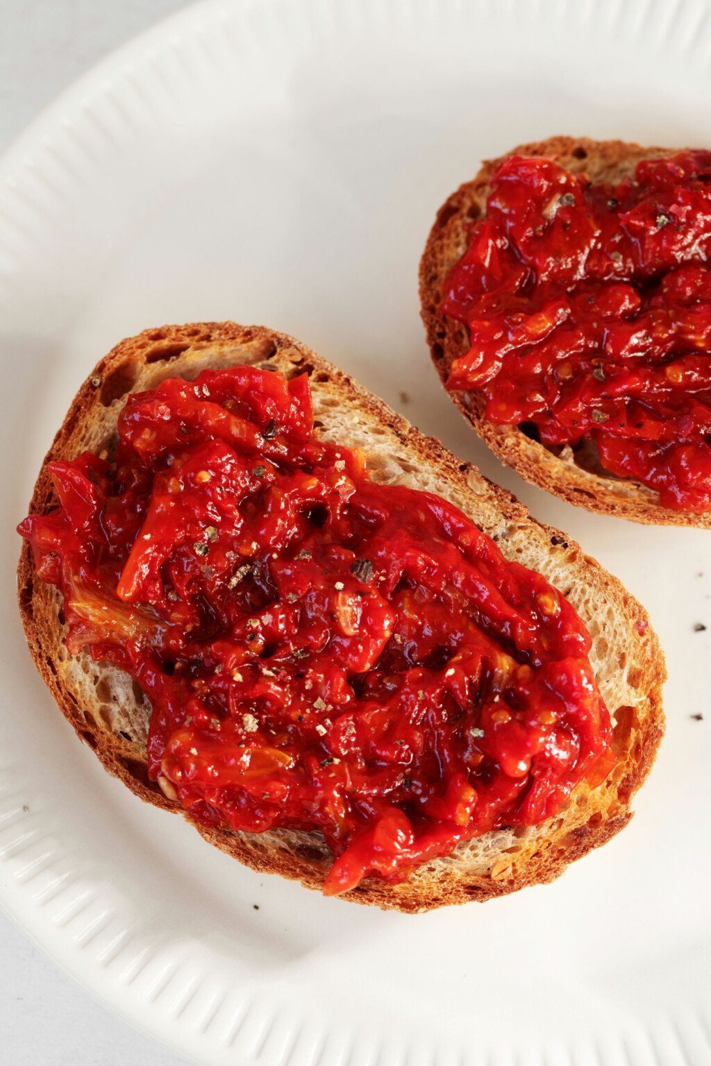 An overhead image of two slices of toast that have been topped with bright red, cherry tomato jam.
