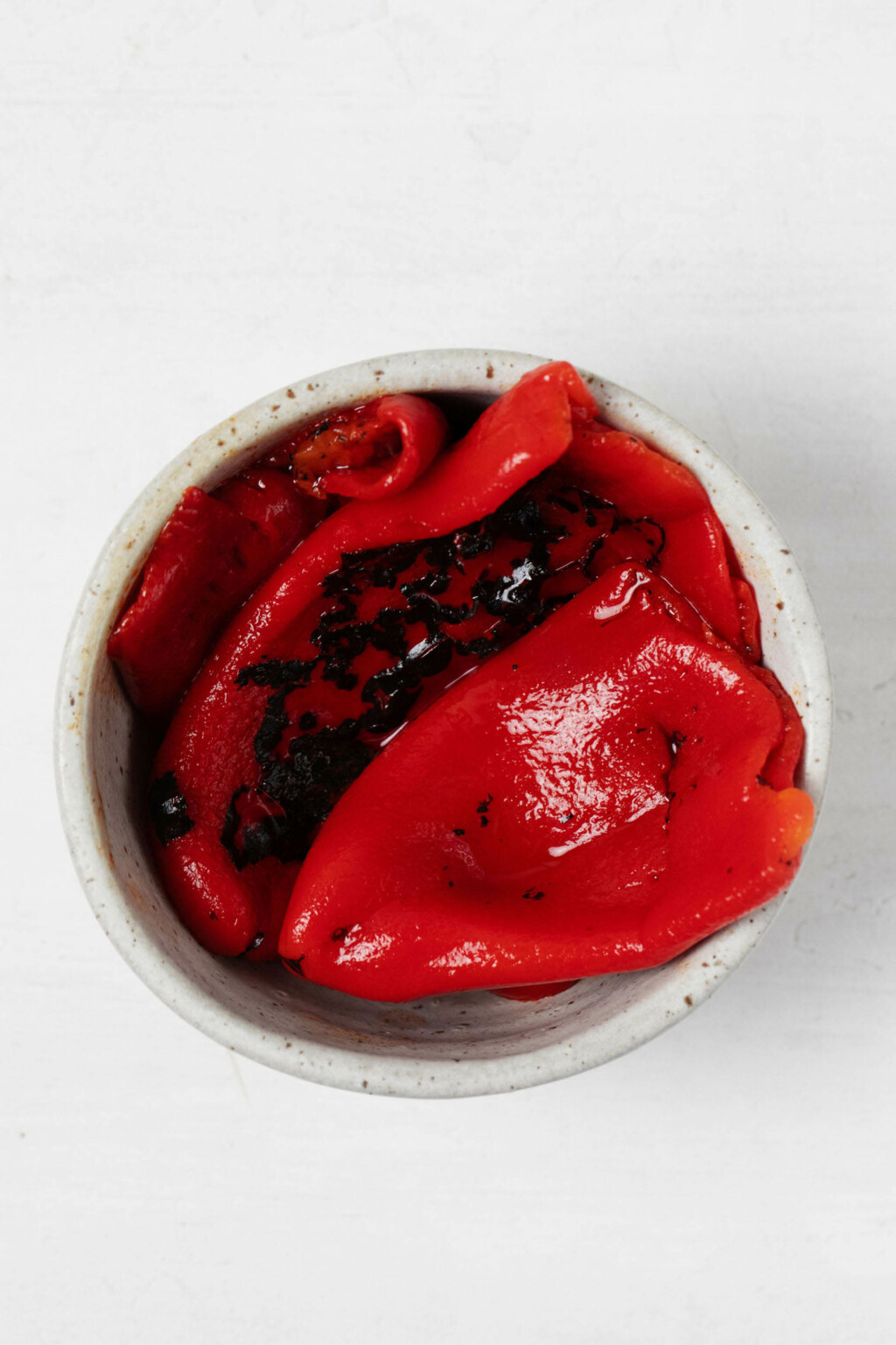 An overhead image of roasted red bell peppers, which are resting in a small pinch bowl.