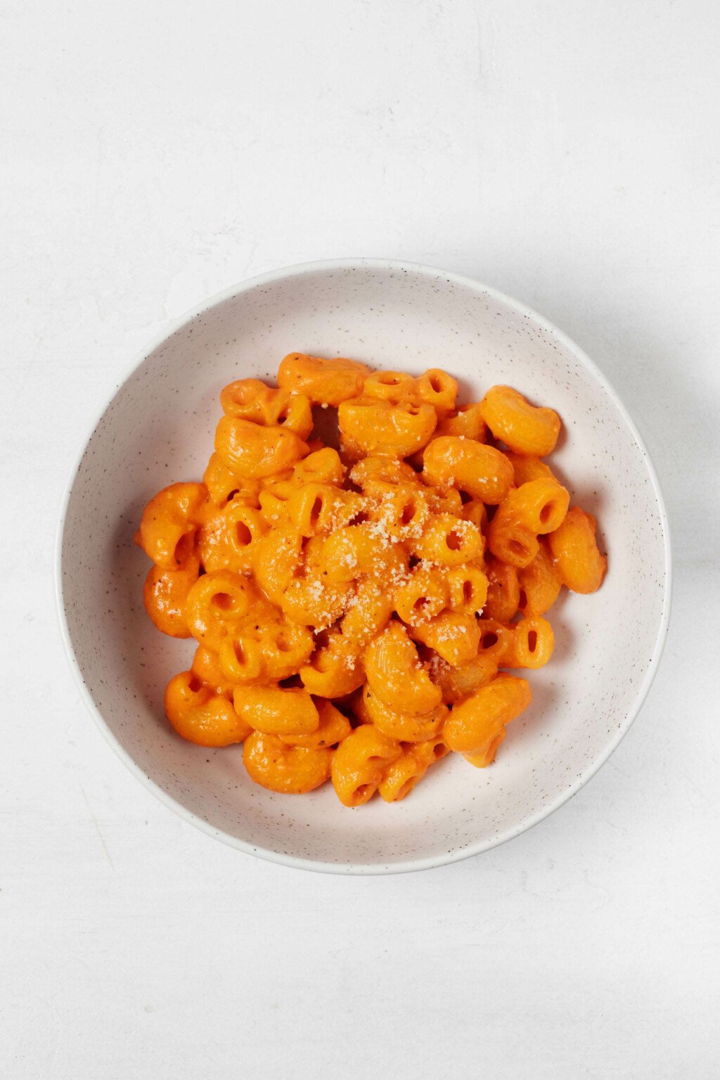 An overhead image of a round, white ceramic bowl, which is filled with a vegan mac and cheese recipe. The color of the pasta sauce is vibrant orange.