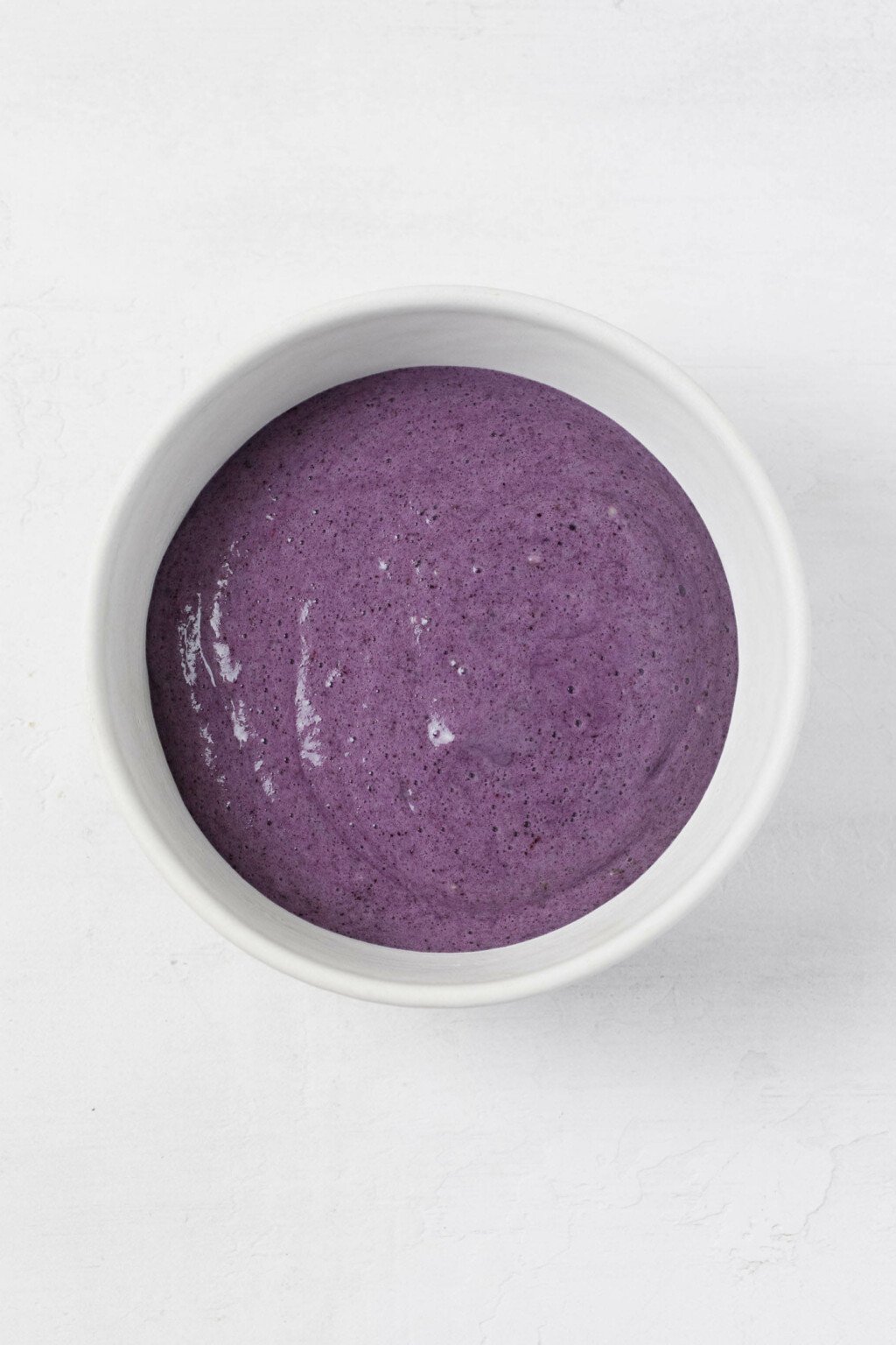 A white bowl rests on a white surface. It contains a frozen purple smoothie.