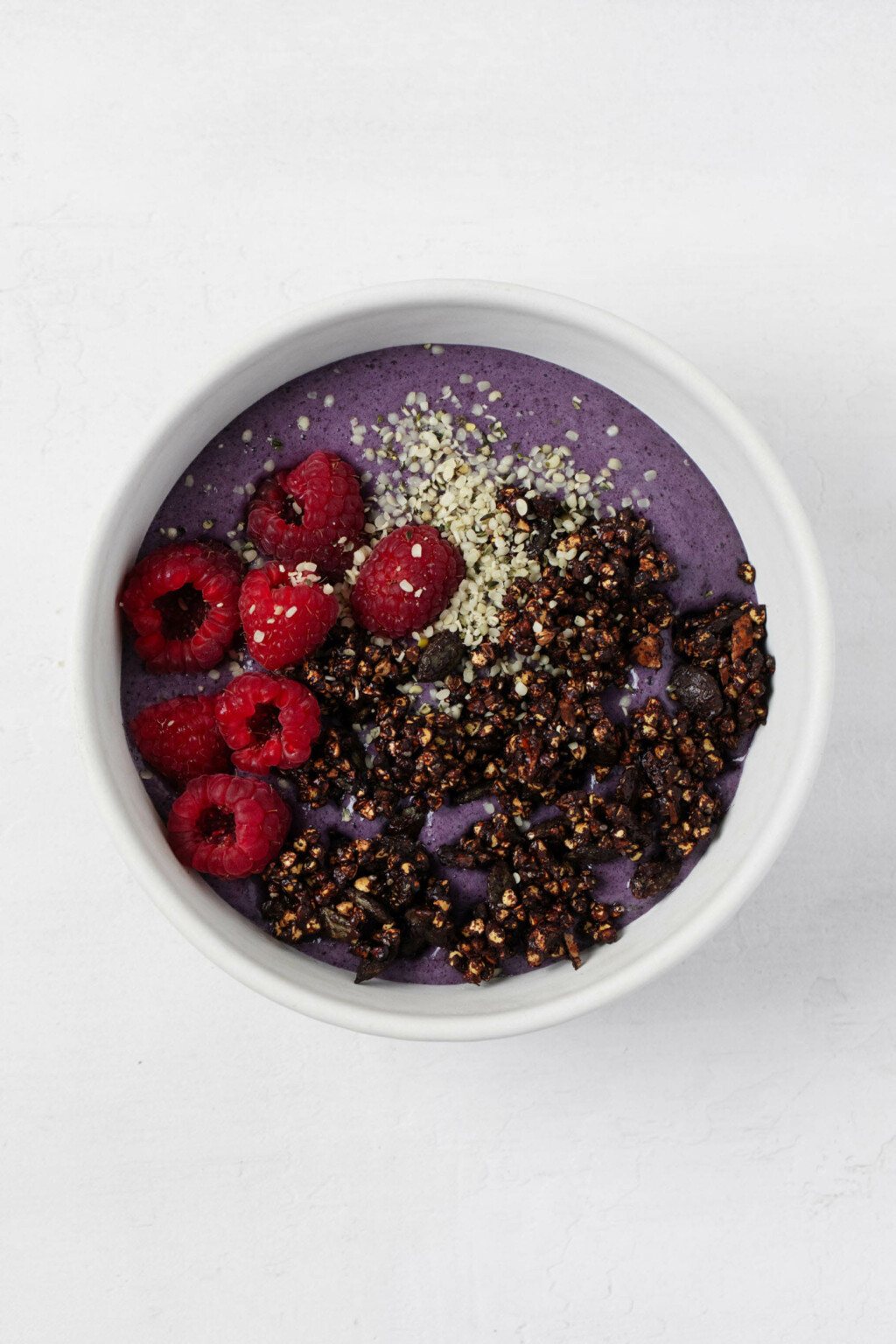 An overhead image of a colorful açaí bowl, which is topped with dark cocoa dusted buckwheat clusters.