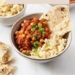 A vegan bean dish with tomatoes is served over a whole grain in a ceramic bowl. It's garnished with chopped parsley.