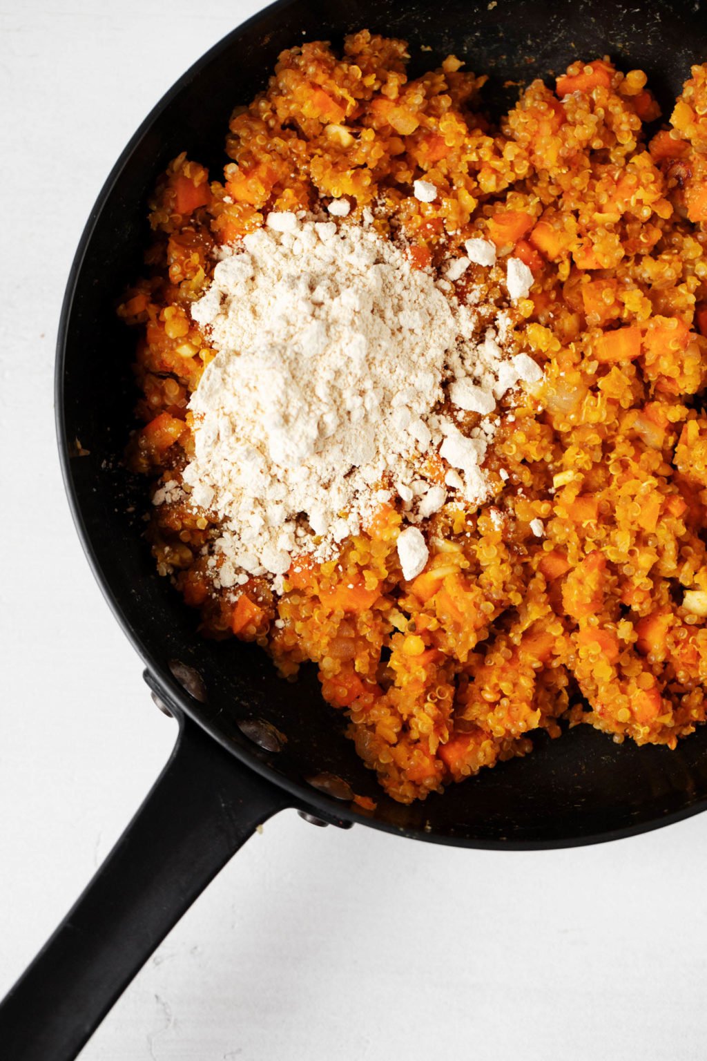 A saucepan has been filled with a cooked mixture of quinoa and red lentils. Dry flour has just been added to the mixture.