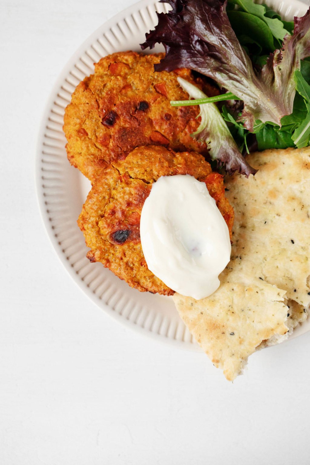 An overhead image of two, orange-hued curried lentil vegetable cakes. They're served with flatbread and greens on a white, rimmed plate.
