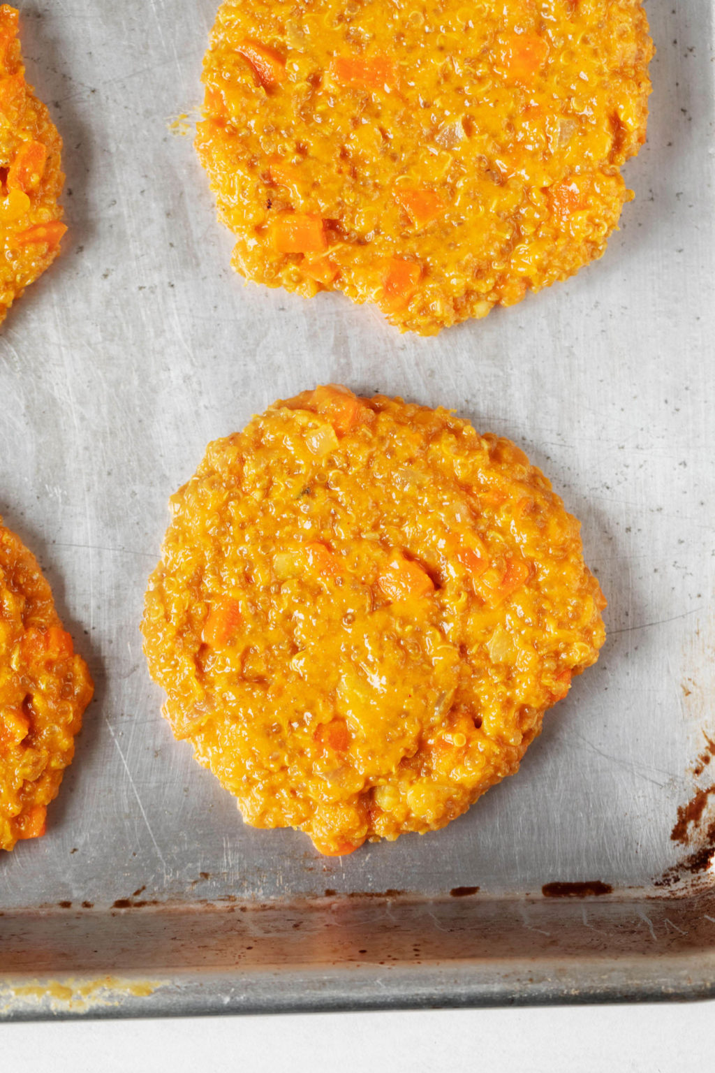 Golden-colored, plant-based patties are resting on a parchment-lined baking sheet, waiting to be baked.