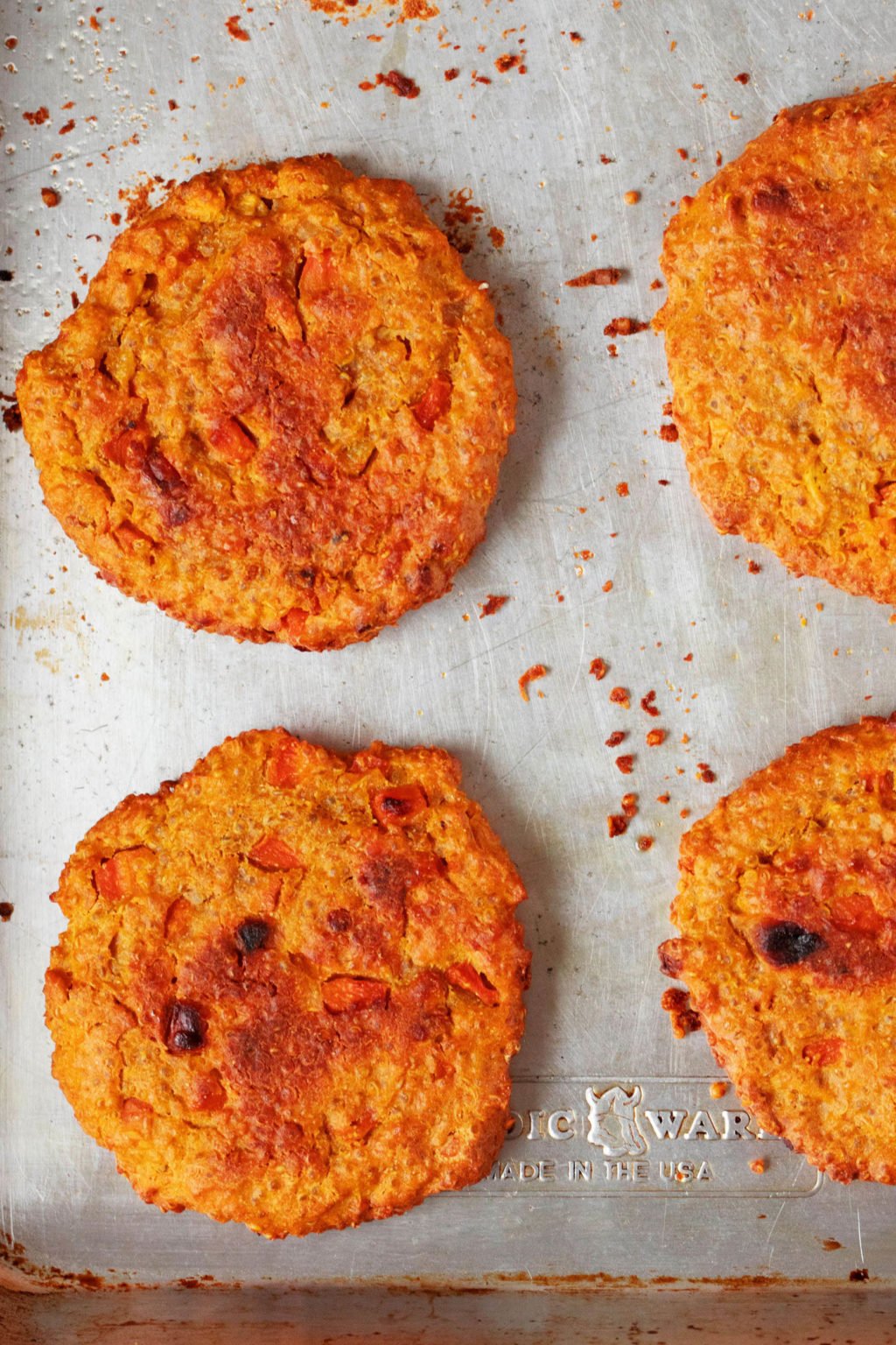 Lightly browning, vegan lentil vegetable cakes have just been taken out of the oven. They're resting on a baking sheet that is lined with white parchment paper.