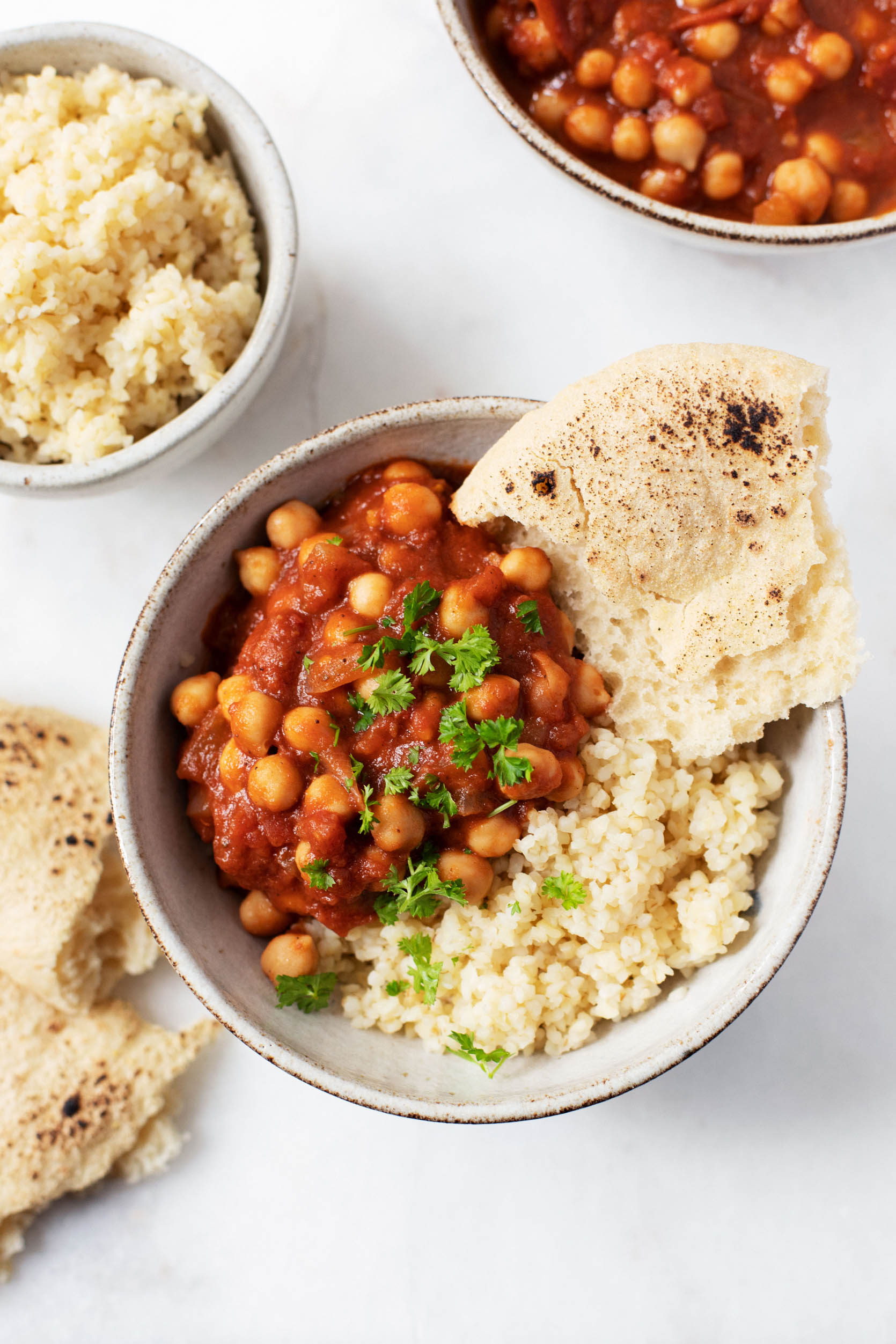 Beans, which are simmered in a spiced sauce, are piled over couscous in a round ceramic serving bowl.