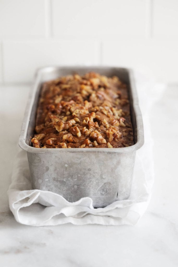 A silver loaf pan holding a freshly baked quick bread that's topped with chopped walnuts..