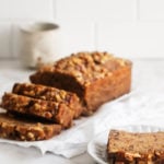 An angled photograph of classic vegan banana bread, sliced and ready to serve