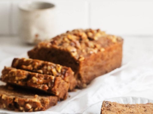 An angled photograph of classic vegan banana bread, sliced and ready to serve