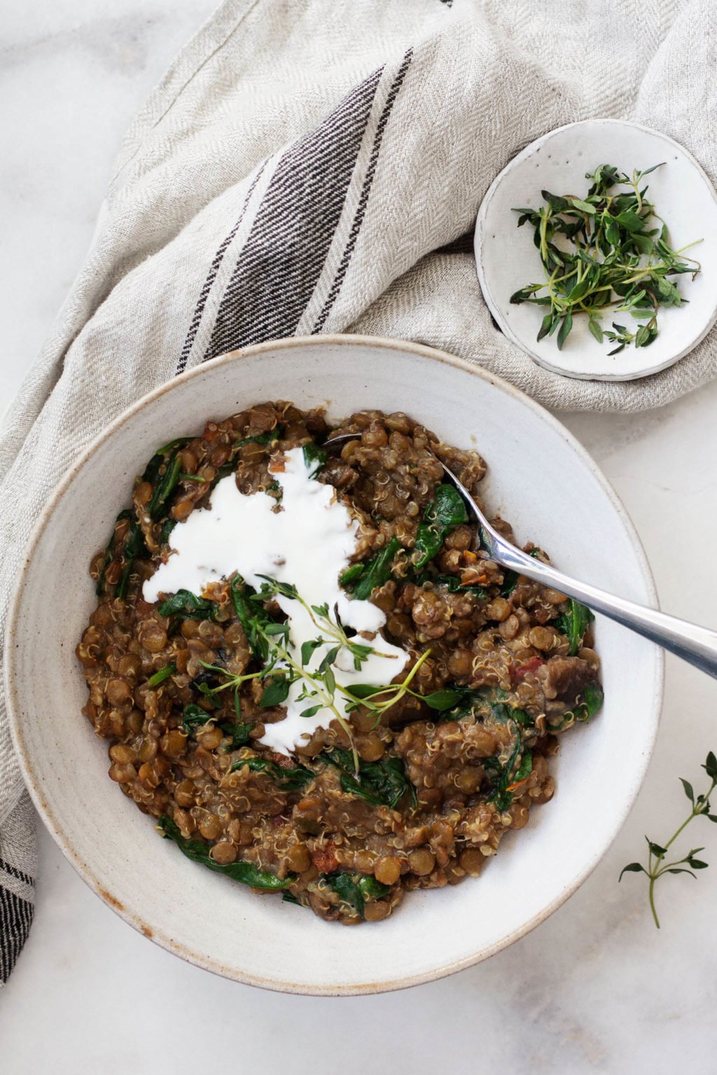 A dish of vegan quinoa and lentils is adorned with a dollop of white cashew cream and some sprigs of thyme.