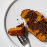 An overhead shot of a piece of pumpkin chocolate marble loaf on a serving plate, with a bite ready to be eaten.