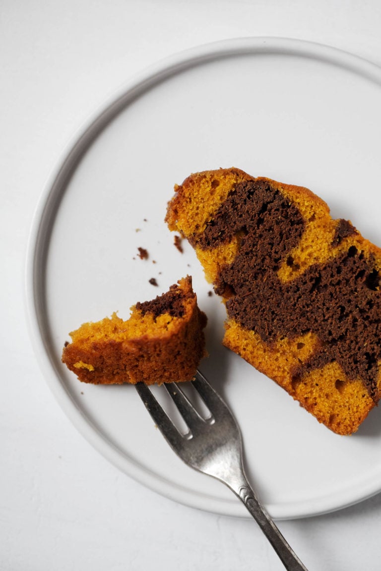 An overhead shot of a piece of pumpkin chocolate marble loaf on a serving plate, with a bite ready to be eaten.