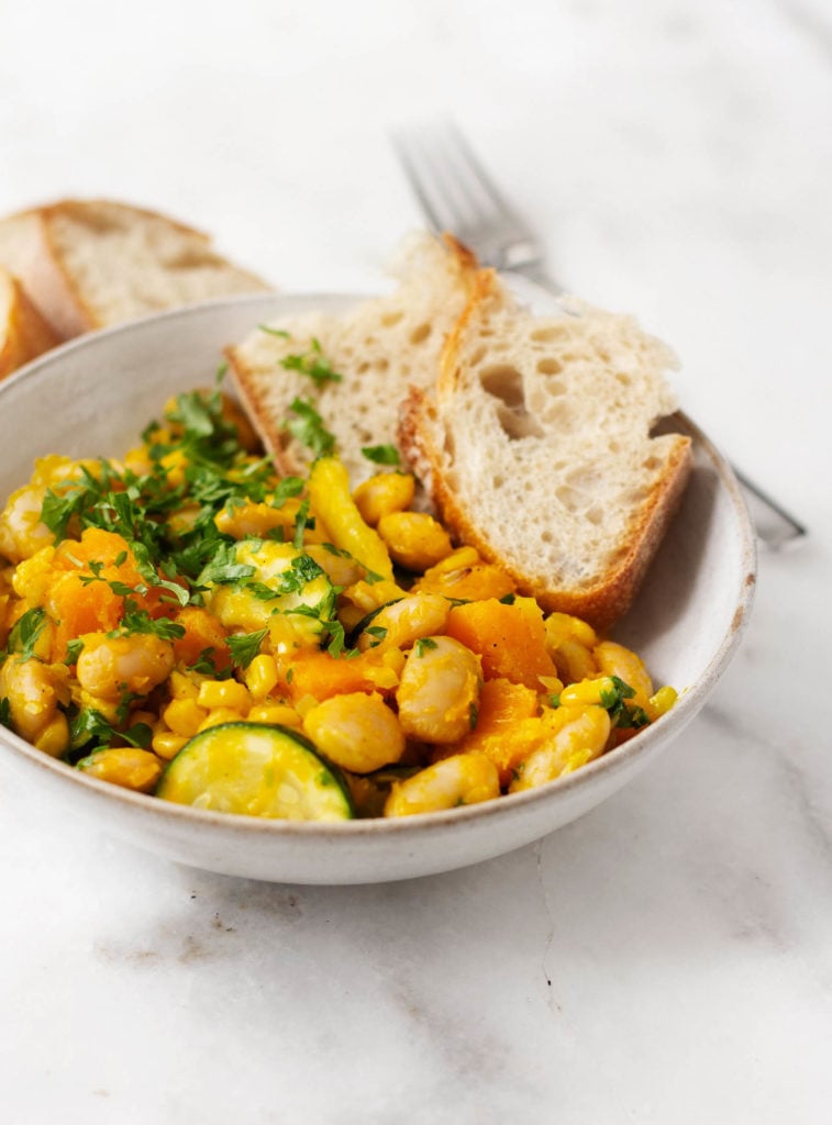 A bowl of golden succotash with butternut squash and lima beans. Served with slices of toast.