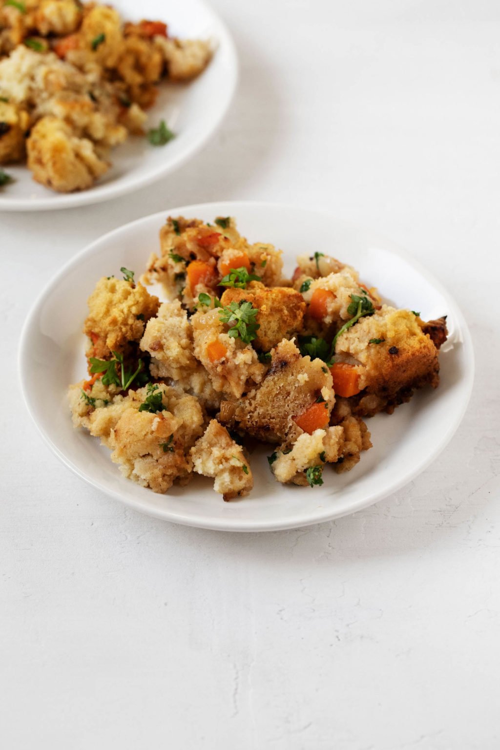 Two plates, topped with vegan cornbread stuffing and herbs.