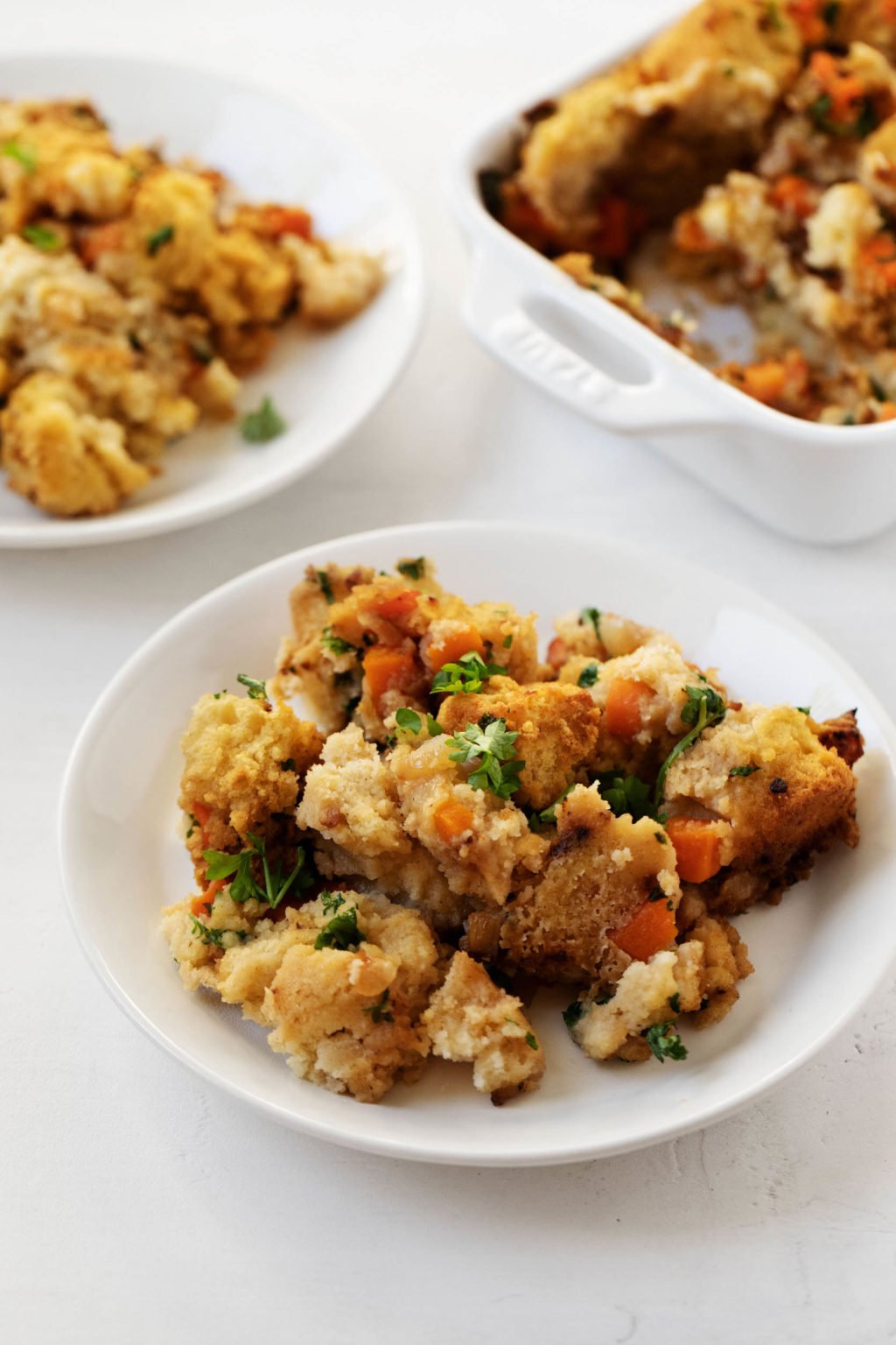 A small plate of vegan cornbread sage stuffing, with another plate and a baking dish in the background.
