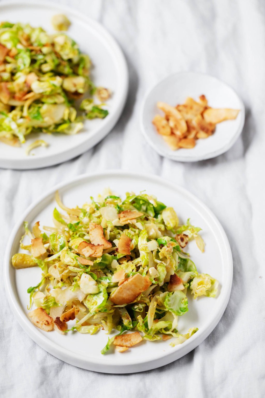 Two side plates of Brussels sprout hash, each topped with vegan coconut bacon.