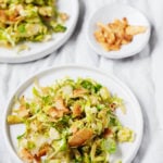 Two side plates of Brussels sprout hash, each topped with vegan coconut bacon.