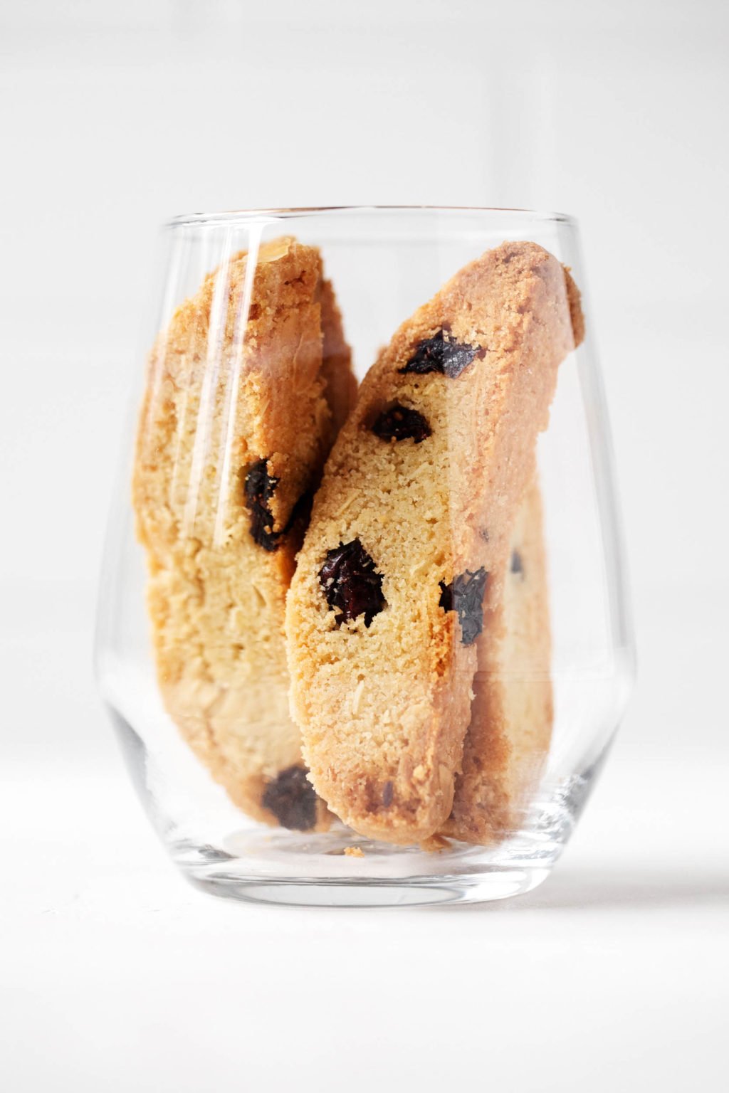 A clear glass holds several vegan cranberry almond biscotti.