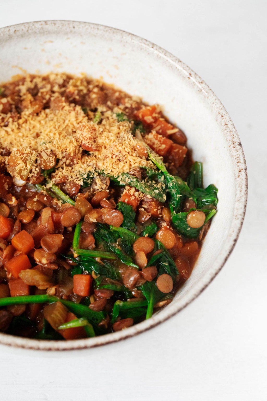 A hearty bowl of lentils, greens, vegetables and crushed cashews is served in a white bowl.