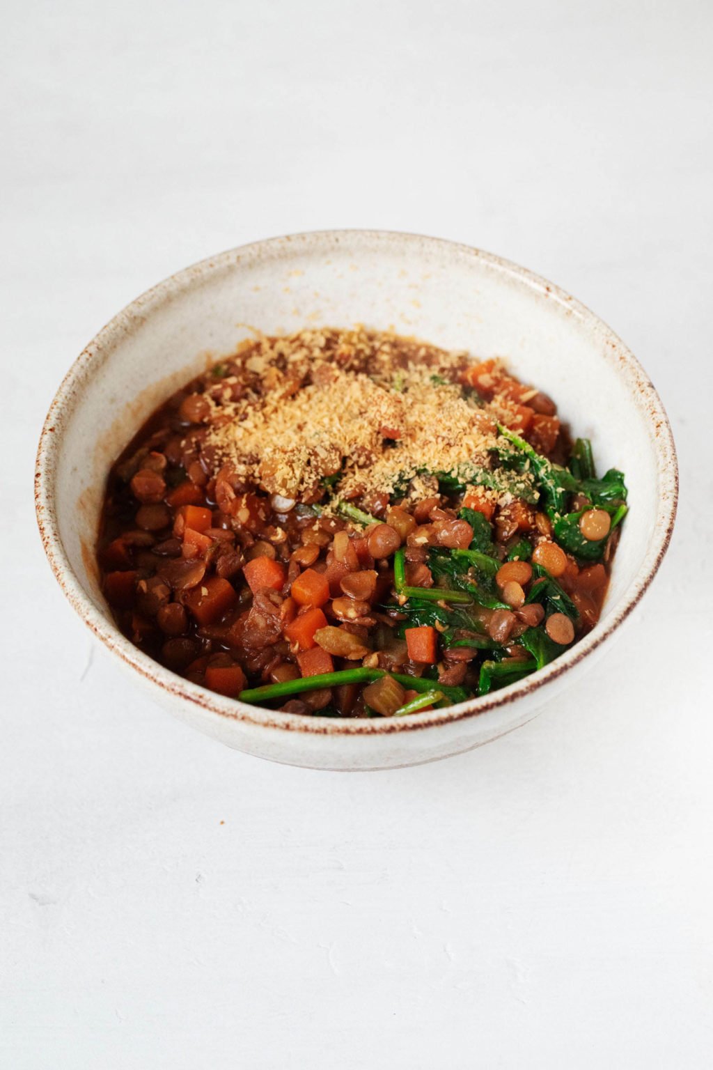 A cream colored soup bowl has been filled with a plant-based, French lentil soup.