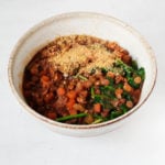 A cream colored soup bowl has been filled with a plant-based, French lentil soup.