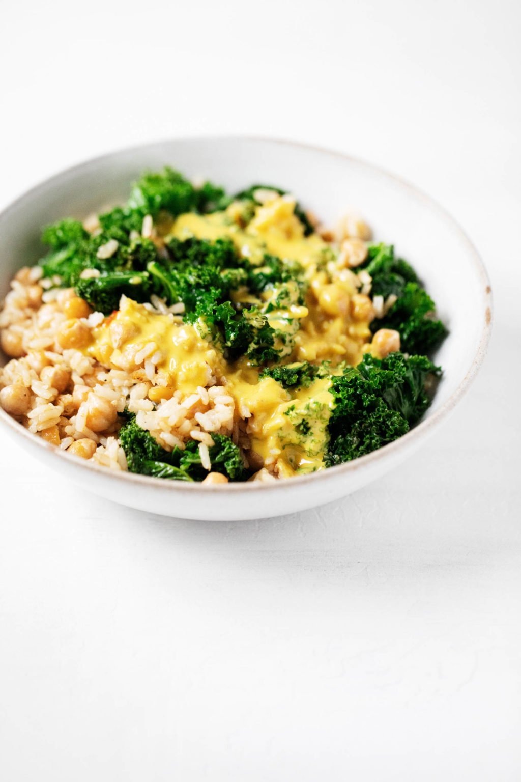 An angled photograph of a bowl of whole grains, beans, and greens, which have been dressed with a golden-hued, creamy sauce.