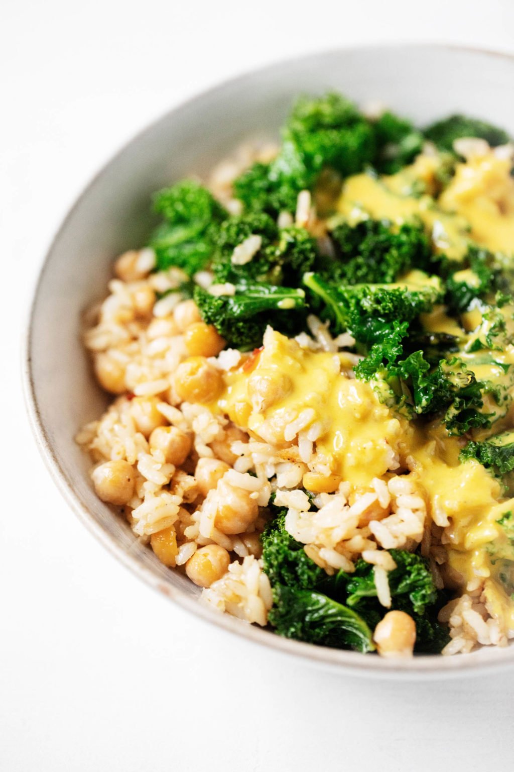 A serving bowl holds colorful plant-based ingredients, dressed in a golden, creamy sauce.